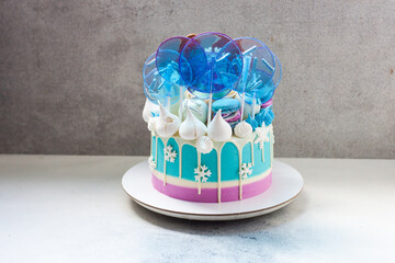 Blue winter cake with white chocolate, lollipops and fondant snowflakes. Grey background.