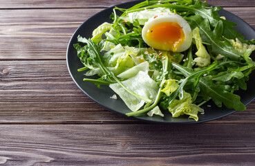 Fresh green salad with egg on dark plate. Wooden dark backdrop. Healthy food concept.