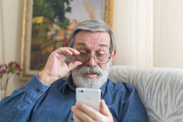 Senior man with beard trying to see the screen of his smartphone.