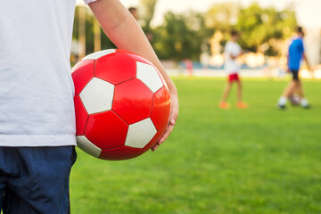 A boy stands on the football field of the stadium and holds a soccer ball against the background of...