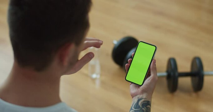 Close up caucasian athletic man making video call on smartphone. Strong fit male calling, talking on phone with green screen, chroma key, waving hand. Self-isolation, internet communication concept.