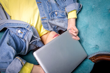 the laptop lies on the girl’s face. girl on a sofa in a denim jacket with a laptop