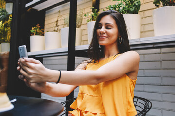 Portrait of beautiful latin woman making self portrait with mobile phone camera while sitting in...