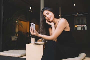 Young latin woman making self portrait on her smartphone digital camera while sitting in sidewalk...