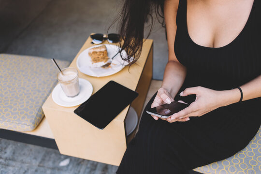 Cropped image of young female chatting on her mobile phone while sitting in coffee shop outdoors, women's hands write text message on telephone in cozy restaurant in the fresh air, wireless connection