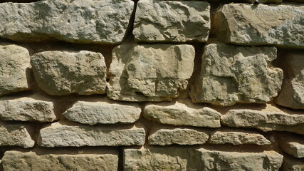 Background: a fragment of a very old wall made up of white and grey stones of various shapes and sizes from the late 19th century.