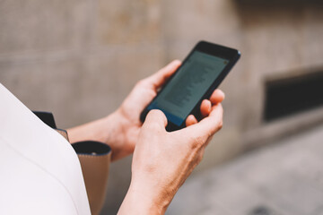 Cropped shot view of female using smart phone with copy space area on the screen while walking on the street in summer day, woman chatting on her cell telephone while strolling around the city