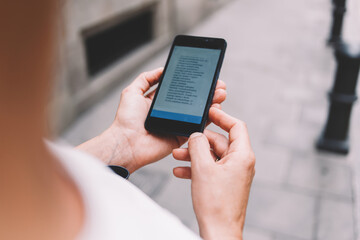 Cropped image of female tourist using mobile phone for navigation while lost way during walking around the city, woman reading text message on cell telephone while strolling outside in urban setting