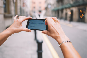 Cropped shot view of woman's hand photographing street view on mobile phone camera for social network picture, female taking picture on her smart phone for mobile chatting while walking on the street