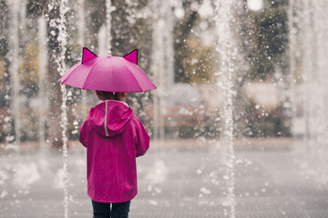 Child girl 4-5 year old wearing raincoat holding umbrella over rain background closeup. Back view....