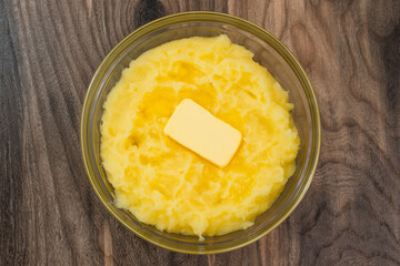 Mushed potato with melting butter close up in a glass bowl on rustic wooden background, directly from above