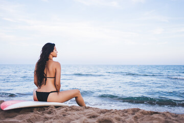 Fototapeta na wymiar Beautiful student is sitting on the beach, relax and enjoy the warm summer days and holiday, attractive woman with long hair scattered on the back sitting on her surfboard and enjoying the sunset