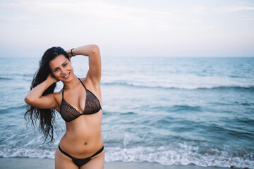 Fototapeta na wymiar Half length portrait of gorgeous latin woman smiling and feeling so good while enjoying her summer vacation holidays, cute charming girl in sexy bikini standing on the shore with copy space area