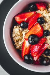 Close up view on oatmeal with strawberries and blueberries on bright textured table