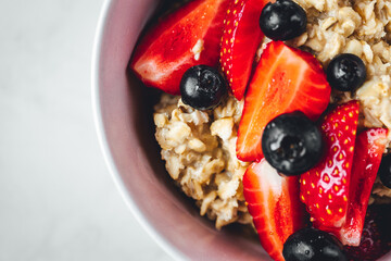 Close up view on oatmeal with strawberries and blueberries on bright textured table