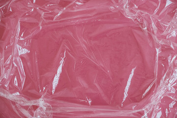 Wrinkled transparent plastic texture on an pink background. Transparent cellophane texture on an...