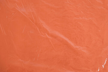 Fototapeta premium Wrinkled transparent plastic texture on an orange background. Transparent cellophane texture on an orange backing. Top view. Copy, empty space for text