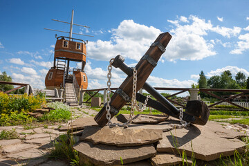 Large anchor as part of the exterior design. Background landscape view with decorative sailboat.  Close-up photo.