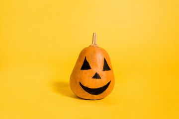 Orange pumpkin with a painted face on a yellow isolated background