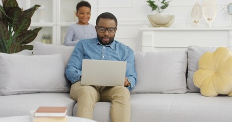 Happy African american man using laptop sitting on sofa at home.