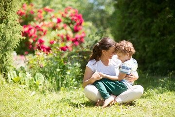 Naklejka na ściany i meble happy Mom and her son sitting in the grass outdoors. Mother with son child having fun togetherss in sunny summer day.