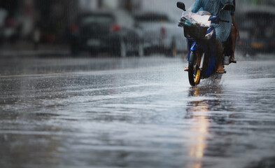 A couple with raincoat on a motorbike during hard rainfall/Dramatic scene of rainy season in...