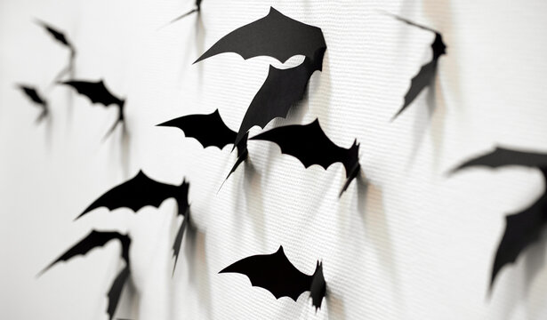 halloween and decoration concept - black paper bats flying over white texture wall
