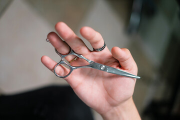 Barber shows scissors for cutting hair close-up. Stylish hairdresser holds scissors in his hand. Rings on the hand.