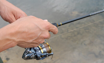 Close-up of a hand holding a spinning rod and turning a reel. A fisherman with a fishing rod. Man fishing. Free time concept.