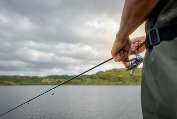 A wading fisherman, with rod and reel, tries to catch a fish in the afternoon. Fishing concept.