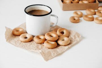 Metal mug with hot drink and mini round bagels on a white wooden background. Copy, empty space for text