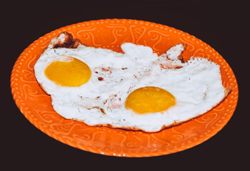 fried eggs on the orange plate, black background.