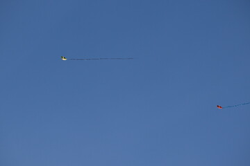 two colored paper kites floating parallel under a cloudless blue sky.