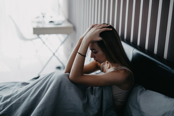 Young sad woman suffering from depression sitting on bed
