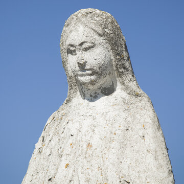 Close up Virgin Mary ancient stone statue against blue sky. Horizontal image.