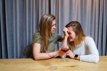 A woman consoles a sad depressed friend who needs help. Depression with alcohol concept. upset young girl with unhappy face holding a glass of wine looking at her best sister