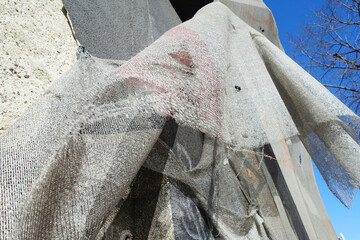 Detail of torn burlap hanging on building, windy day on reconstruction site. Grey rough material...