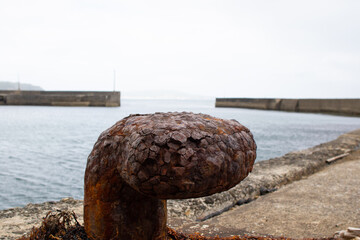 Rusty port mooring block close up with the empty port view in the background. It has a deep brown flaking appearance. Very Rustic in nature.