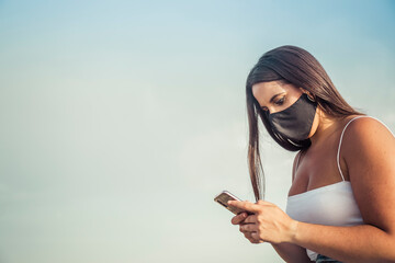 brunette woman with mask looks at her mobile