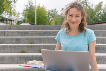 smiling woman sitting on stairs and using laptop computer, studying online