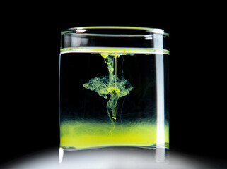 A glass of water on a black background with yellow paint.