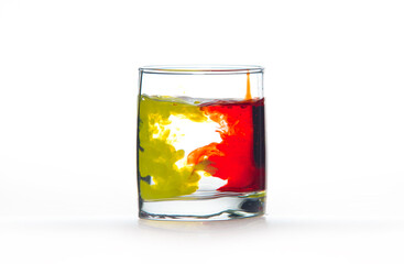 A glass of water on a white background with red and yellow paint.