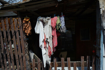 Washed laundry is drying in sun in front of old poor house. Worker's uniform is hanging on wire in old house yard.