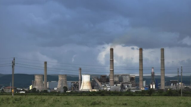 Time lapse of thermal power plant cooling towers and chimney stacks, with storm clouds behind them. CET Govora near Ramnicu Valcea, Romania.