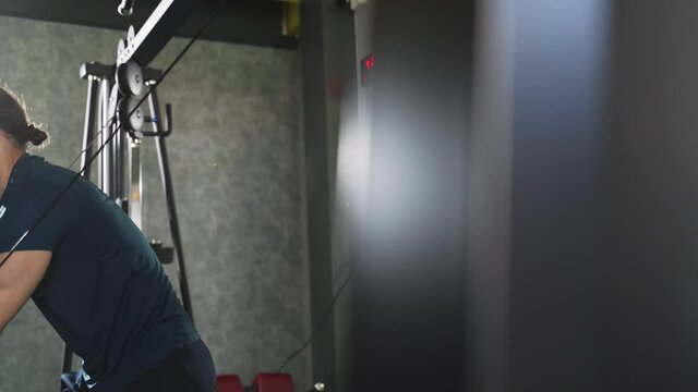 Young man working out in gym pulling weight at cable crossover machine