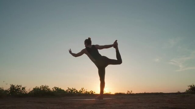 Low angle shot of man standing in dancer yoga pose while practicing outdoors at sunset