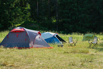 Camping tents and folding chairs in summer forest.