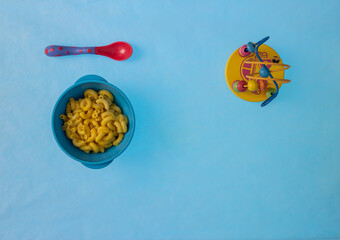 Toddler plate with macaroni and cheese with toy next to the food and a lot of space for copy