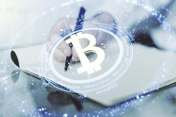 Double exposure of creative Bitcoin symbol with man hand writing in notebook on background. Cryptocurrency concept