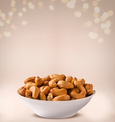 cashew nuts into a bowl on beige background.